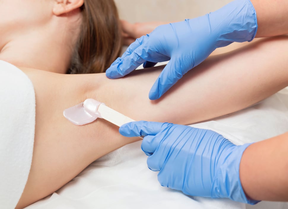 Armpit waxing procedure in a beauty salon. Master applies wax to woman's armpit.